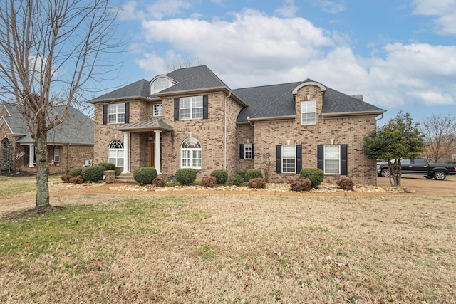 view of front of property featuring brick siding, a shingled roof, and a front yard