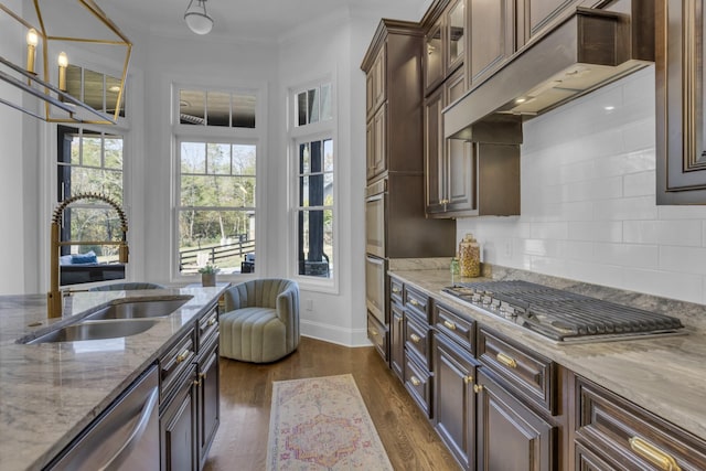 kitchen featuring custom range hood, appliances with stainless steel finishes, light stone countertops, dark brown cabinets, and a sink