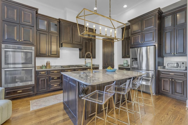 kitchen featuring light stone counters, a breakfast bar area, a sink, appliances with stainless steel finishes, and an island with sink