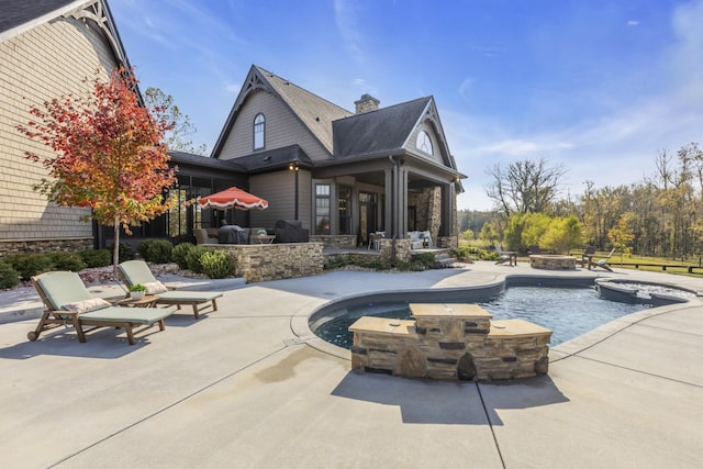 rear view of property with an outdoor fire pit, an outdoor pool, a patio, a chimney, and an in ground hot tub