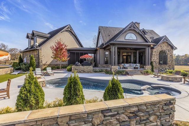 back of house with stone siding, a patio area, an outdoor pool, and a chimney