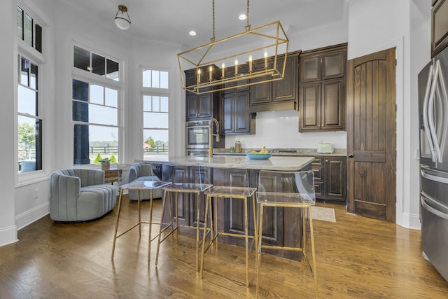 kitchen with an island with sink, dark wood-style floors, a breakfast bar, and dark brown cabinets