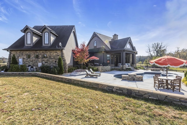 rear view of house featuring a yard, stone siding, a patio area, and an outdoor pool