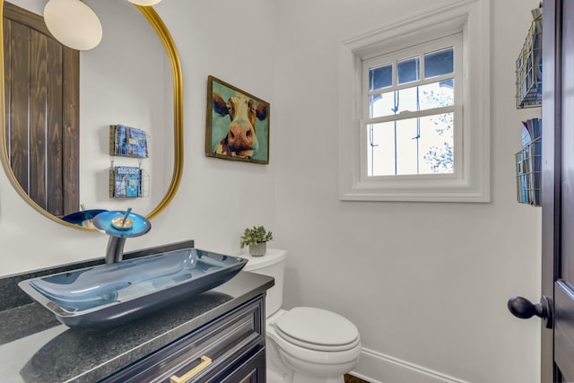 half bathroom featuring toilet, vanity, and baseboards