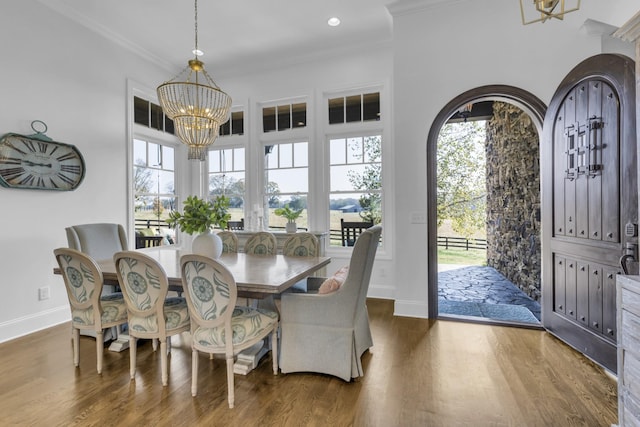 dining room featuring arched walkways, dark wood finished floors, ornamental molding, a chandelier, and baseboards