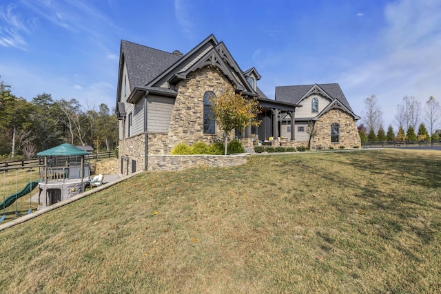 view of front of house featuring stone siding, a playground, fence, and a front lawn