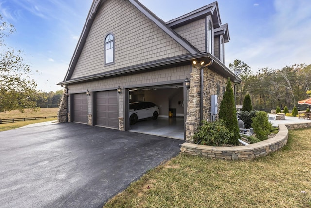 view of side of property featuring aphalt driveway, stone siding, a lawn, and a garage