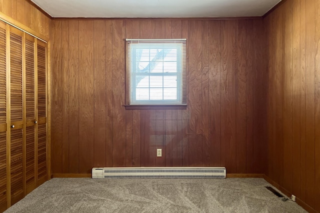 empty room with a baseboard heating unit, carpet, visible vents, and wooden walls