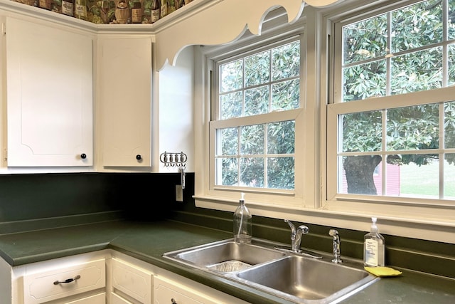 kitchen featuring plenty of natural light, dark countertops, white cabinets, and a sink