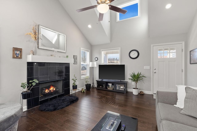 living area featuring baseboards, a ceiling fan, dark wood-style floors, a fireplace, and high vaulted ceiling