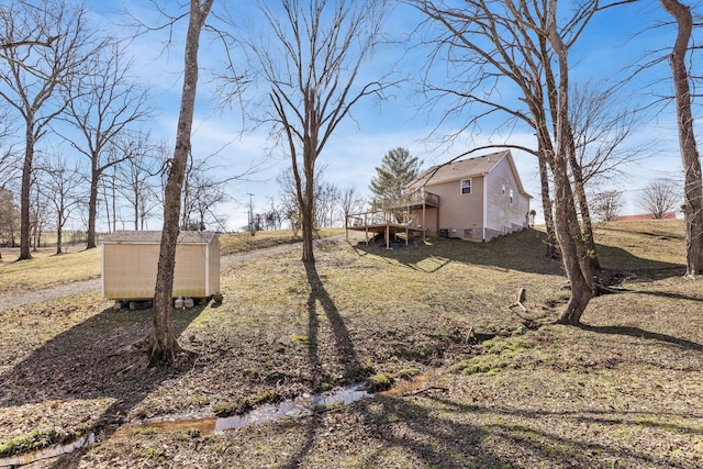 view of yard with a shed, a rural view, a wooden deck, and an outbuilding