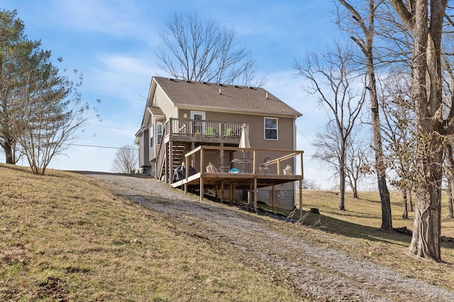 back of property featuring a deck, dirt driveway, a lawn, and stairs