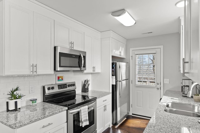 kitchen with appliances with stainless steel finishes, dark wood-type flooring, light stone countertops, white cabinetry, and a sink