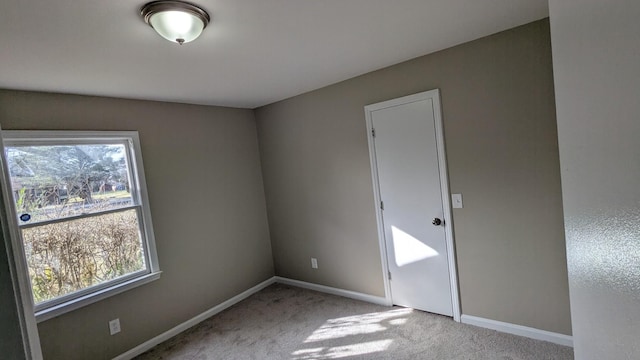 empty room with a healthy amount of sunlight, baseboards, and light colored carpet