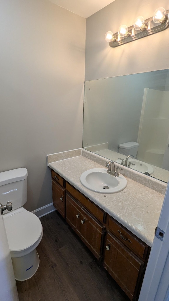 bathroom featuring toilet, baseboards, wood finished floors, and vanity