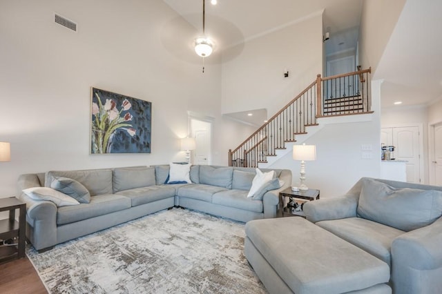 living room with visible vents, ornamental molding, wood finished floors, a high ceiling, and stairs