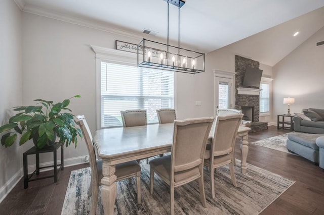 dining space featuring visible vents, dark wood-type flooring, vaulted ceiling, a stone fireplace, and baseboards