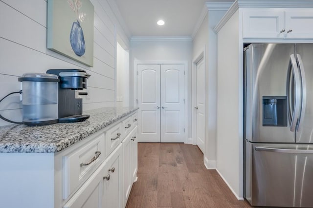 kitchen featuring wood finished floors, ornamental molding, white cabinetry, light stone countertops, and stainless steel fridge