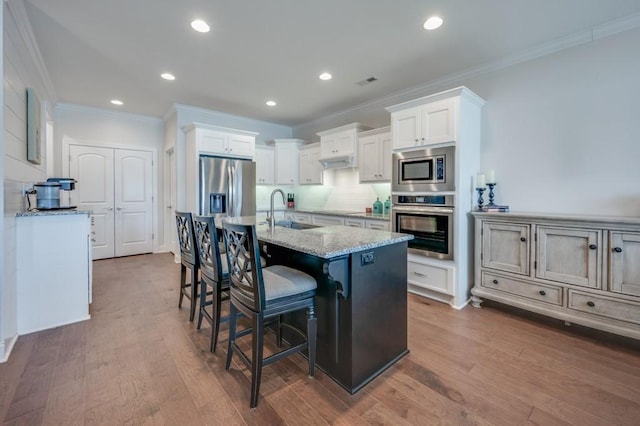 kitchen featuring a sink, white cabinetry, appliances with stainless steel finishes, light stone countertops, and a center island with sink