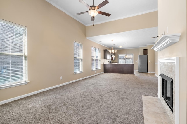 unfurnished living room featuring a brick fireplace, ceiling fan with notable chandelier, ornamental molding, and light colored carpet