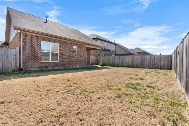 rear view of house featuring roof with shingles, brick siding, a lawn, and a fenced backyard