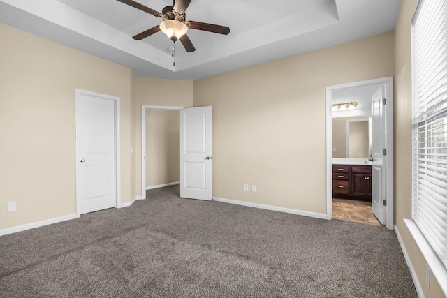 unfurnished bedroom with ensuite bathroom, carpet floors, a tray ceiling, and baseboards