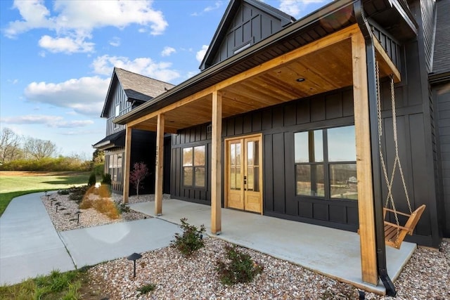 exterior space with a patio area, french doors, board and batten siding, and roof with shingles