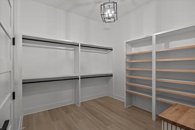 spacious closet featuring light wood-type flooring and a notable chandelier