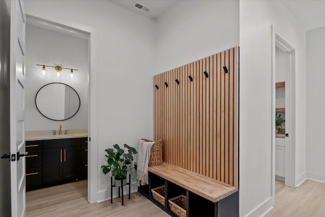 mudroom with light wood finished floors, baseboards, visible vents, and a sink