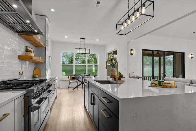 kitchen with a kitchen island with sink, a sink, exhaust hood, appliances with stainless steel finishes, and decorative light fixtures