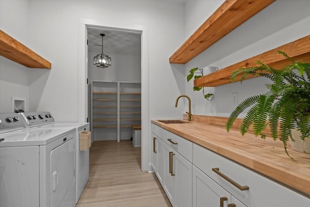 laundry room with cabinet space, light wood-type flooring, a chandelier, separate washer and dryer, and a sink