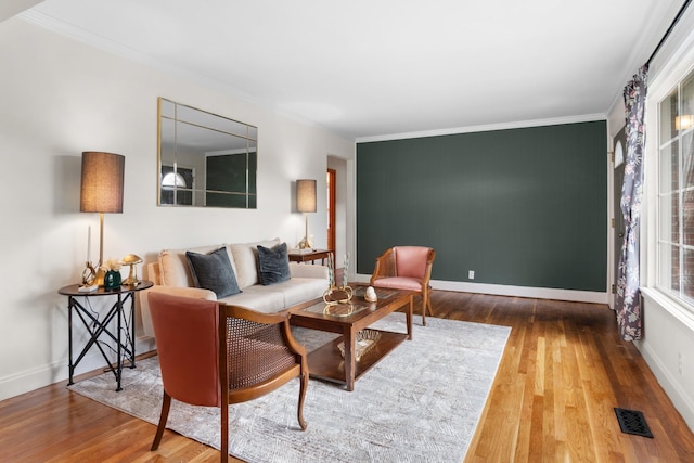 living room with ornamental molding, wood finished floors, visible vents, and baseboards