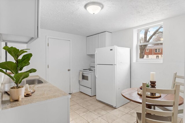 kitchen featuring a textured ceiling, light tile patterned flooring, white appliances, white cabinets, and light countertops