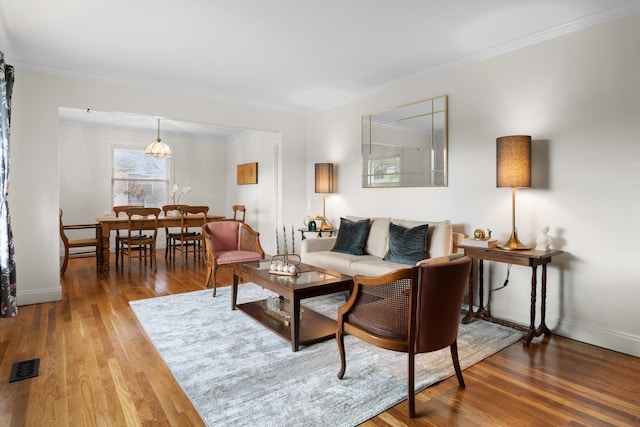 living area with baseboards, crown molding, visible vents, and wood finished floors