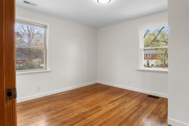 spare room featuring baseboards, light wood-style flooring, visible vents, and crown molding