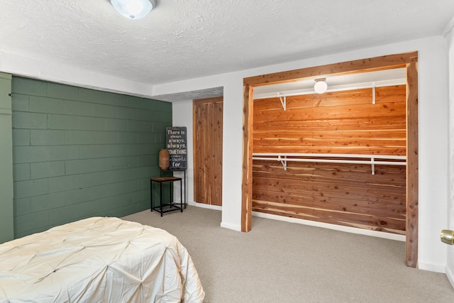 bedroom with carpet floors, concrete block wall, a textured ceiling, and baseboards