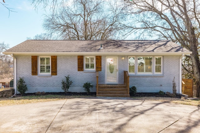 ranch-style house featuring a shingled roof, entry steps, and brick siding