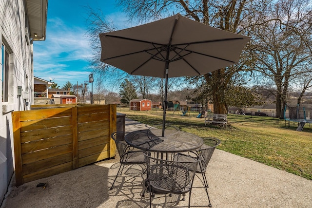 view of patio featuring an outbuilding, a storage shed, fence, outdoor dining space, and a trampoline