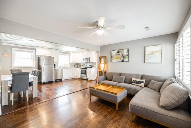 living area with a ceiling fan, visible vents, and dark wood-type flooring