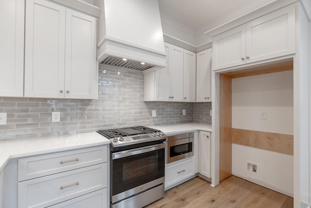 kitchen featuring tasteful backsplash, custom exhaust hood, stainless steel appliances, light countertops, and white cabinetry