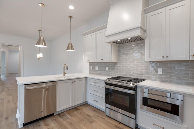 kitchen featuring pendant lighting, light countertops, appliances with stainless steel finishes, a sink, and premium range hood