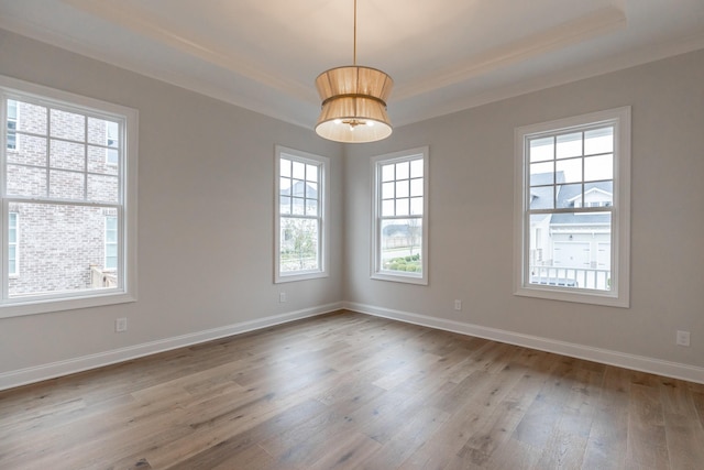 spare room with crown molding, a raised ceiling, light wood-style flooring, and baseboards