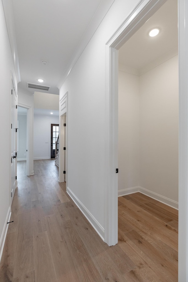 hall with light wood-style floors, baseboards, visible vents, and crown molding