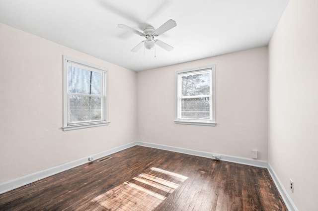 spare room with dark wood-style floors, baseboards, visible vents, and a wealth of natural light