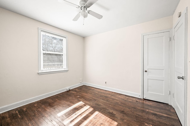 spare room featuring dark wood-style floors, a ceiling fan, and baseboards