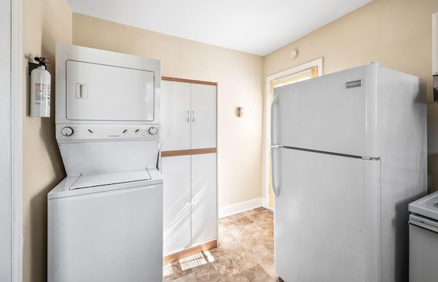 clothes washing area featuring stacked washing maching and dryer and baseboards