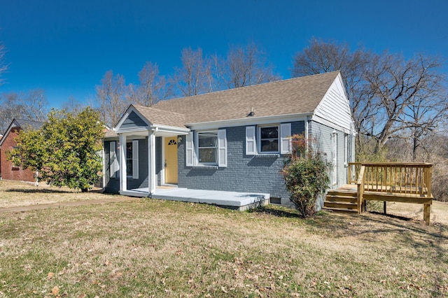 view of front facade featuring a wooden deck, roof with shingles, a front lawn, and brick siding