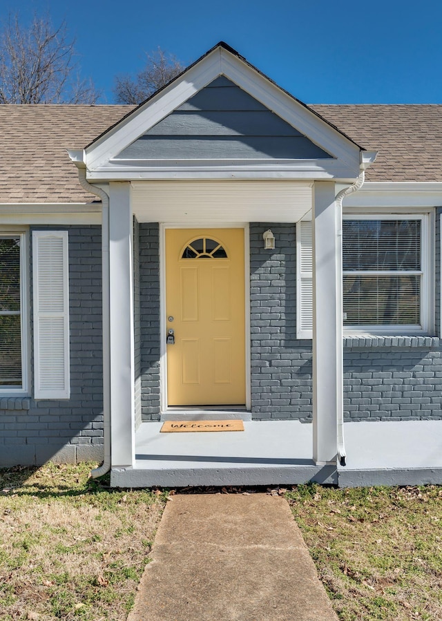 doorway to property with brick siding and roof with shingles