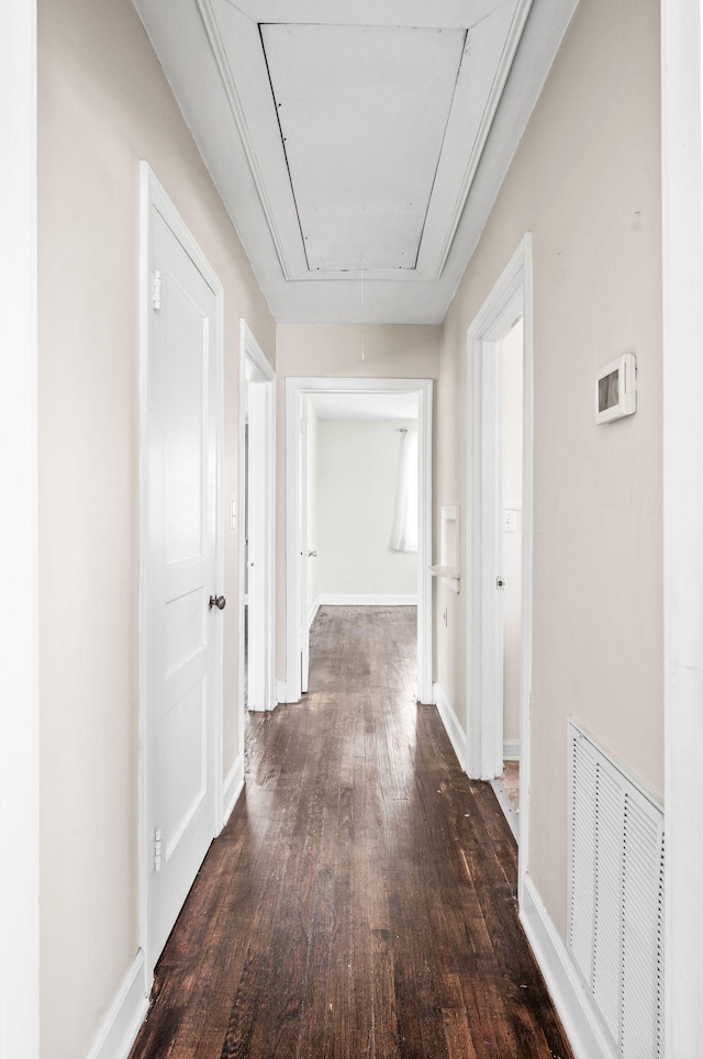 hall featuring dark wood-style floors, baseboards, visible vents, and attic access