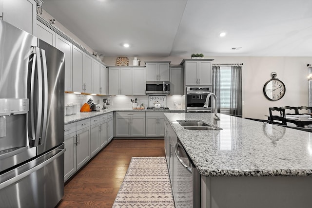 kitchen with stainless steel appliances, an island with sink, a sink, and gray cabinetry